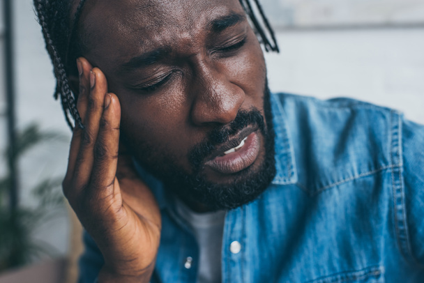 unglücklicher afrikanisch-amerikanischer Mann hält Hand in Kopfnähe, während er unter Kopfschmerzen leidet - Foto, Bild
