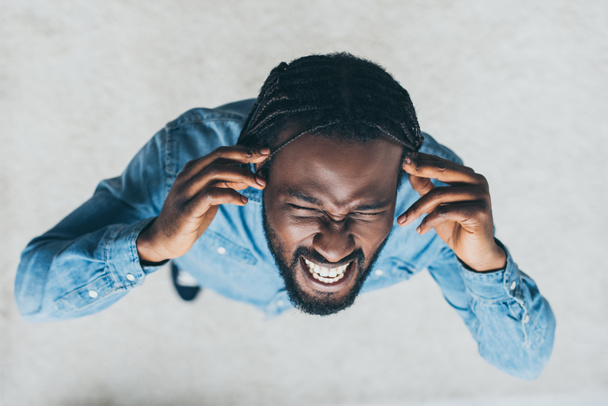 bovenaanzicht van Afrikaanse man handen in de buurt van hoofd terwijl lijdt aan hoofdpijn - Foto, afbeelding