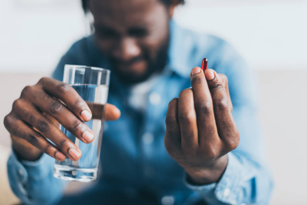 selective focus of african american man suffering from hurt and holding glass of water and pill - Foto, Imagem