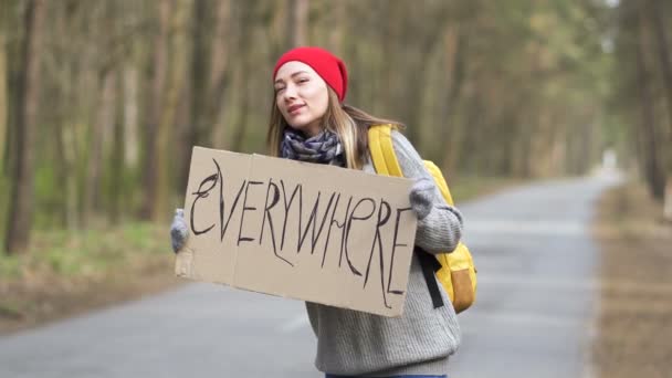 Fiatal csinos stoppoló nő állni az úton poszterrel Mindenhol. Várakozó autó érzelem  - Felvétel, videó
