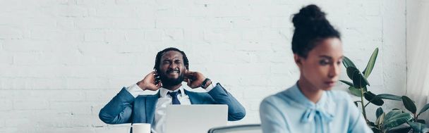 plan panoramique de manager afro-américain souffrant de maux de tête alors qu'il était assis au bureau près d'une jolie femme d'affaires
  - Photo, image