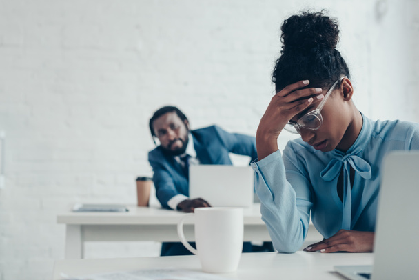 exhausted businesswoman suffering from headache while sitting in office near colleague - Fotó, kép