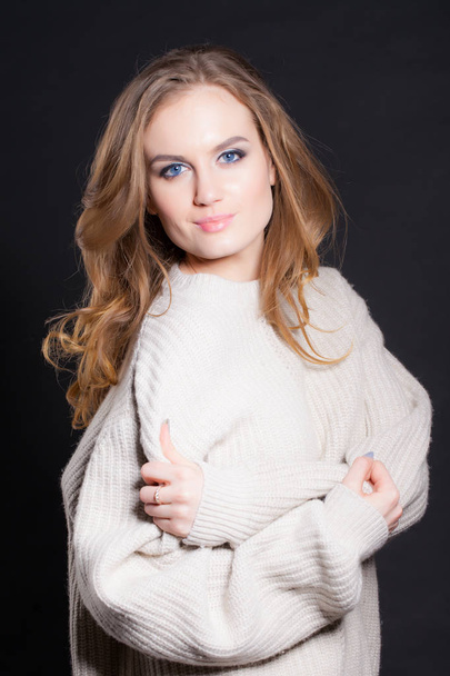 portrait of a young, beautiful woman on a black background in a large sweater - Photo, Image