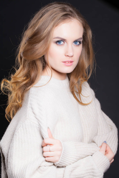 portrait of a young, beautiful woman on a black background in a large sweater - Foto, imagen
