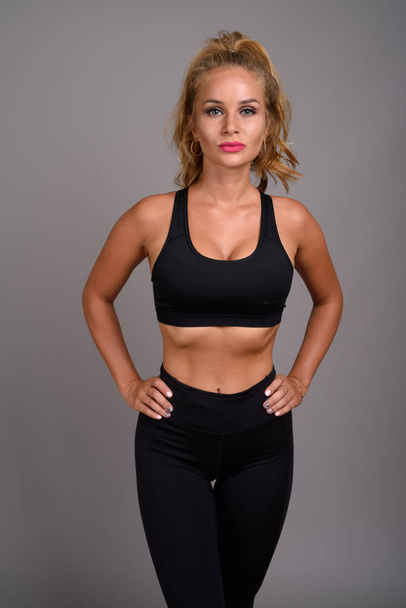 Young beautiful woman with blond hair ready for gym against gray - Photo, Image