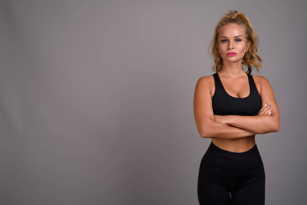 Young beautiful woman with blond hair ready for gym against gray - Fotó, kép