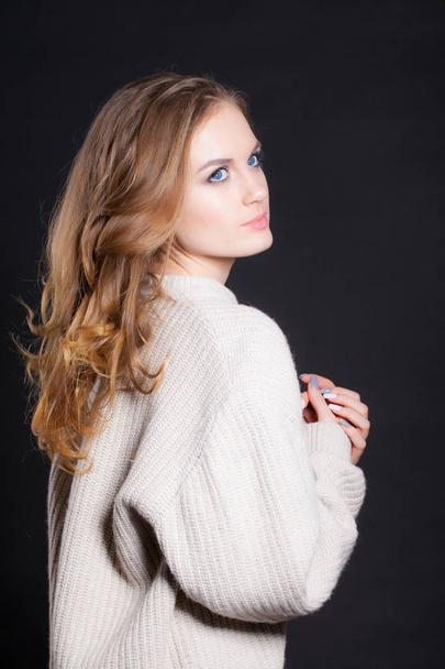 portrait of a young, beautiful woman on a black background in a large sweater - Foto, Imagem