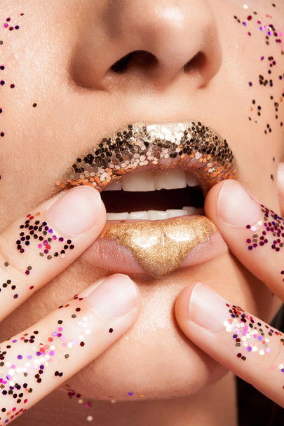Woman with golden lips and glitter on her hands in studio - Photo, Image