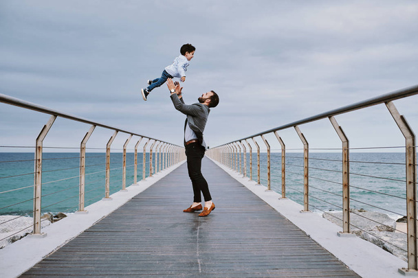 un padre joven en un puente con su hijo volando encima de él
 - Foto, Imagen