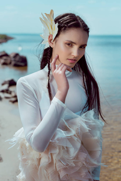 Sahilde durmuş kameraya bakan beyaz kuğu kostümlü genç bir kadın. - Fotoğraf, Görsel