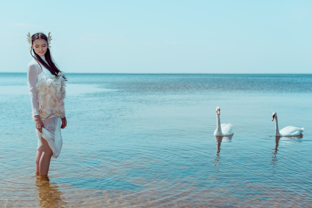 mulher adulta em traje de cisne branco em pé no rio perto de pássaros
 - Foto, Imagem