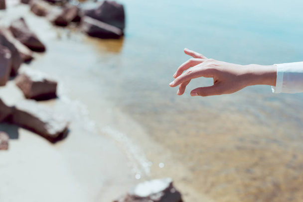 cropped view of woman hand on beach and river background - 写真・画像