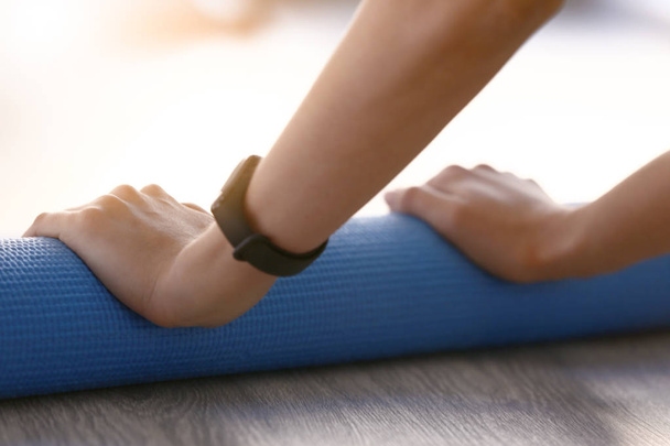 Young woman rolling out yoga mat in gym, closeup - Foto, afbeelding