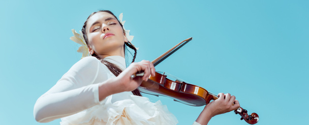 низький кут зору ніжної жінки в білому лебединому костюмі, що стоїть на фоні блакитного неба зі скрипкою
 - Фото, зображення