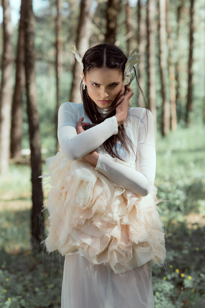 adult woman in white swan costume standing on forest background, holding hands near face - Photo, Image