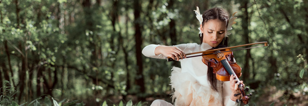 Panoramablick auf brünette Frau im weißen Schwanenkostüm, die auf Geige spielt - Foto, Bild