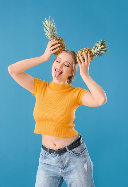Grappige jonge vrouw met ananassen op kleur achtergrond - Foto, afbeelding