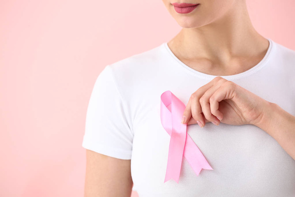 色の背景にピンクリボンを持つ若い女性。乳がんの認知概念 - 写真・画像