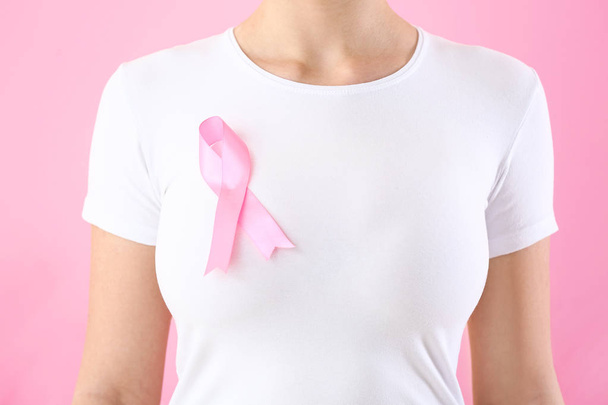 Young woman with pink ribbon on color background. Breast cancer awareness concept - 写真・画像