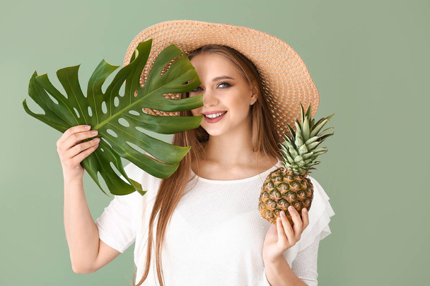 Beautiful young woman with pineapple and tropical leaf on color background - Photo, Image