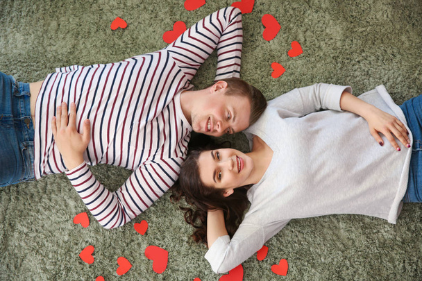 Feliz pareja joven con corazones de papel acostados en la alfombra
 - Foto, imagen