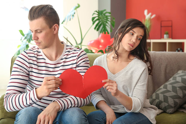 Ένα δυστυχισμένο νεαρό ζευγάρι που διαλύει την καρδιά του χαρτιού στο σπίτι. Σύγκρουση σε σχέση - Φωτογραφία, εικόνα