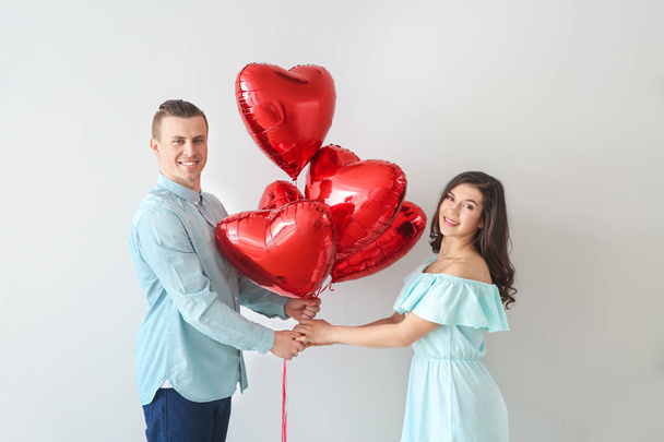 Ευτυχισμένο νεαρό ζευγάρι με μπαλόνια αέρα σε ανοιχτόχρωμο φόντο - Φωτογραφία, εικόνα