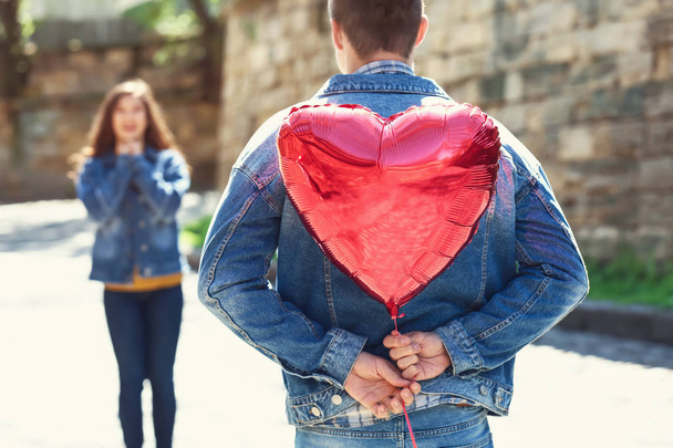 Mladý muž skrývá srdce ve tvaru vzduchový balón pro přítelkyni za jeho zády venku - Fotografie, Obrázek