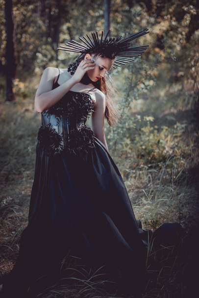 mujer adulta en traje de bruja negro de pie sobre el fondo del bosque, mirando hacia otro lado
 - Foto, imagen