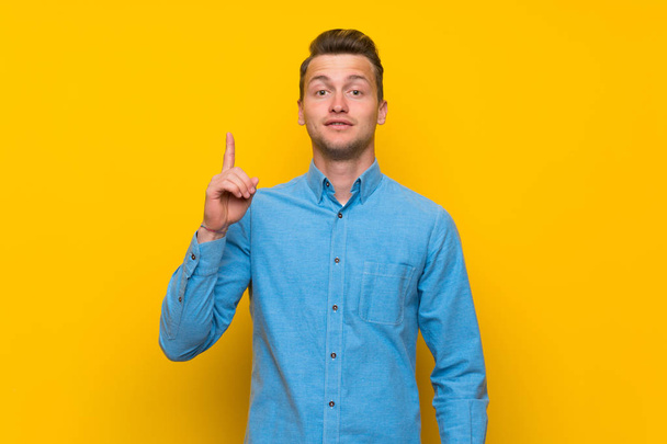 Hombre rubio sobre aislada pared amarilla pensando en una idea apuntando con el dedo hacia arriba
 - Foto, Imagen