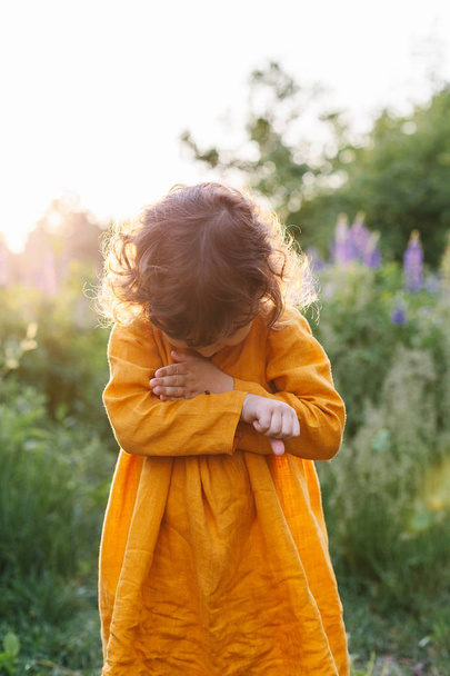 Adorabile bambina vestita in lino senape con coccinella tra i fiori di lupino
 - Foto, immagini