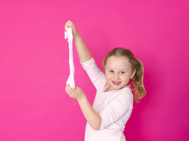 beautiful blonde little girl playing with slime in front of pink background - Фото, изображение