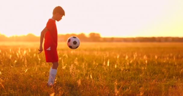 Niño jugador de fútbol al atardecer haciendo malabares con la pelota en el campo
 - Imágenes, Vídeo