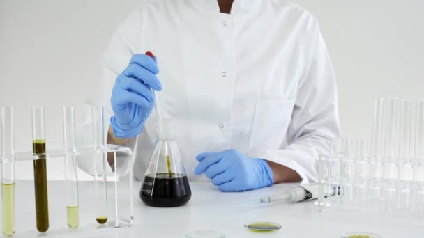 実験室で女性科学者は、マリファナ植物から抽出Cbd油をテストします。彼女は実験にガラスのドロッパーとチューブを使っている。医療大麻からのヘルスケア薬局. - 映像、動画