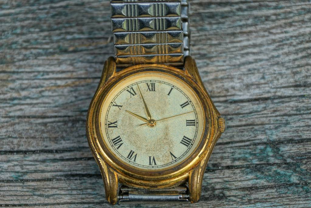 un viejo reloj de mala calidad amarillo con una correa de metal en una mesa gris
 - Foto, Imagen