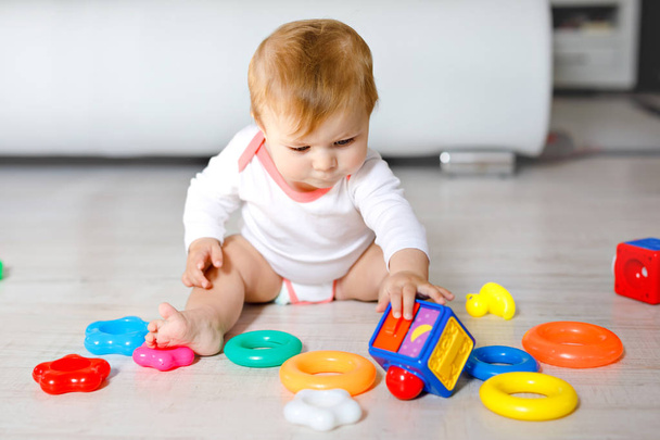Adorable baby girl playing with educational toys in nursery. Happy healthy child having fun with colorful different toys at home. Kid trying to build plastic pyramid and using blocks with letters - Foto, immagini