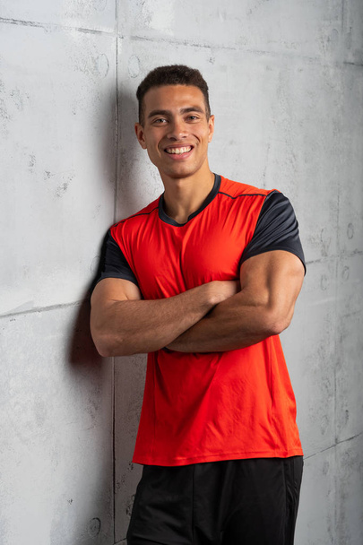 Young sporty man in red t-shirt posing on grey concrete background  - Φωτογραφία, εικόνα