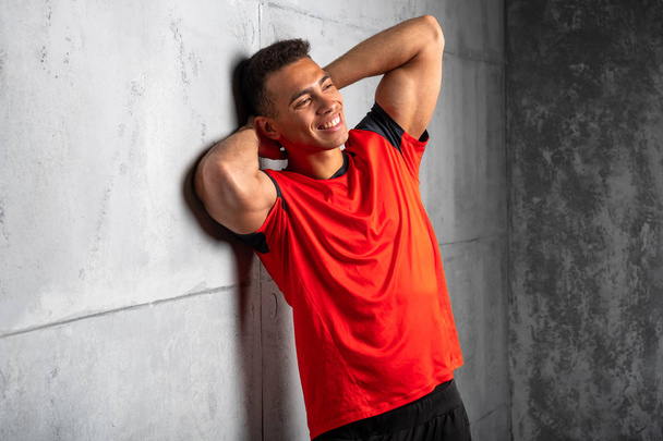 Young sporty man in red t-shirt posing on grey concrete background  - Fotó, kép