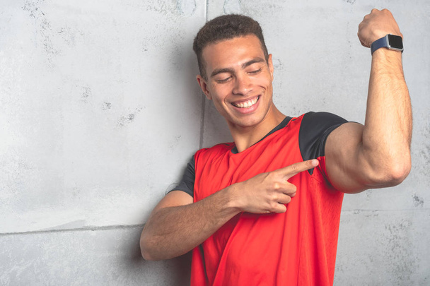Young sporty man in red t-shirt posing on grey concrete background  - Foto, Imagen