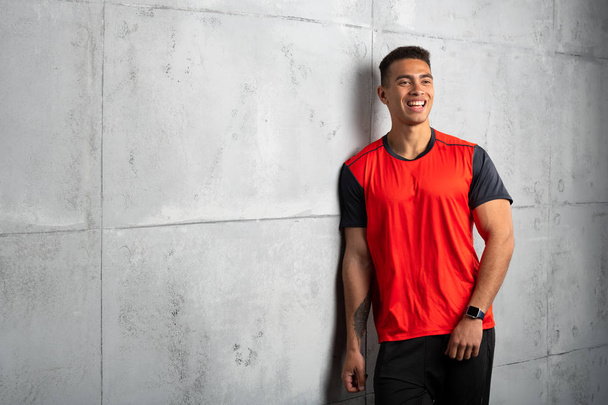Young sporty man in red t-shirt posing on grey concrete background  - Zdjęcie, obraz