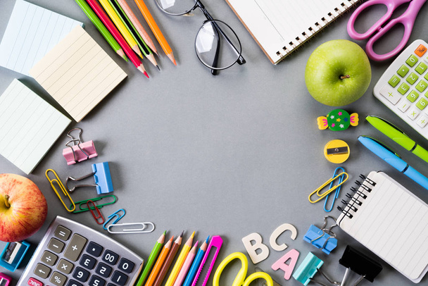 Education or back to school Concept. Top view of Colorful school supplies with books, color pencils, calculator, pen cutter clips and green apple on gray background. Flat lay. - Photo, Image