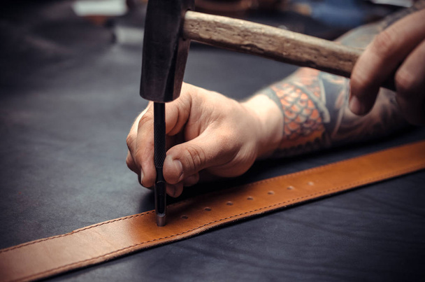 Handicraftsman processing a leather workpiece at the workshelf - Photo, Image
