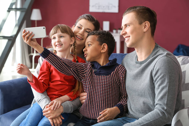 Onnellinen pari adoptoitujen lasten kanssa, jotka ottavat selfien kotona
 - Valokuva, kuva