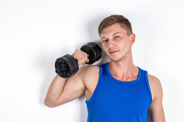 Handsome young man in blue shirt lifting dumbbell. White background - Fotoğraf, Görsel