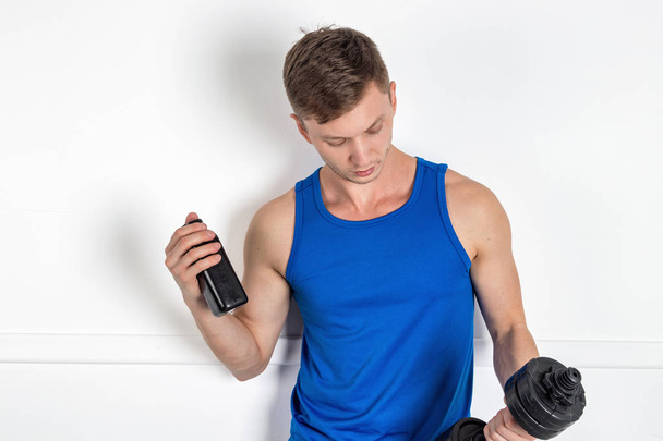 Handsome young man in blue shirt lifting dumbbell. Sport and sports nutrition - Foto, Bild