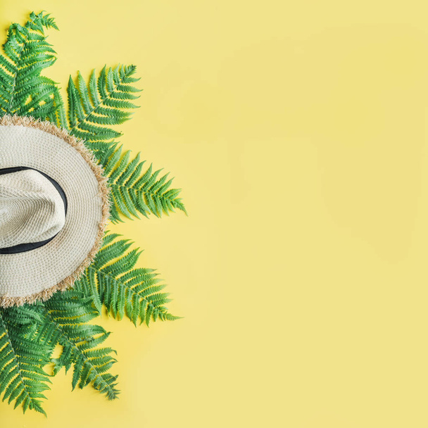 Female beach straw sunhat and fern leaves on yellow. Top view. Summer travel concept. - Photo, Image