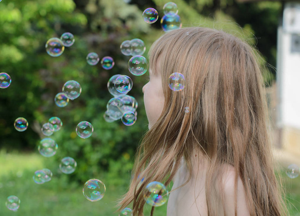 Menina joga e gosta de bolhas de sabão no pátio
 - Foto, Imagem