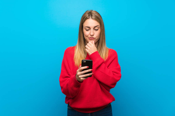 Mujer con suéter rojo sobre pared azul pensando y enviando un mensaje
 - Foto, imagen