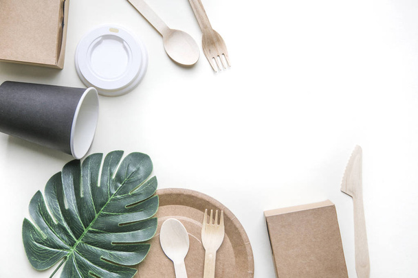 eco friendly disposable dishes made paper on white marble background. Draped spoons, fork, knives, plate with paper cups. recycling concept - Фото, изображение