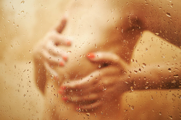 Blurred view on sexy girl in shower behind wet glass . - Foto, afbeelding